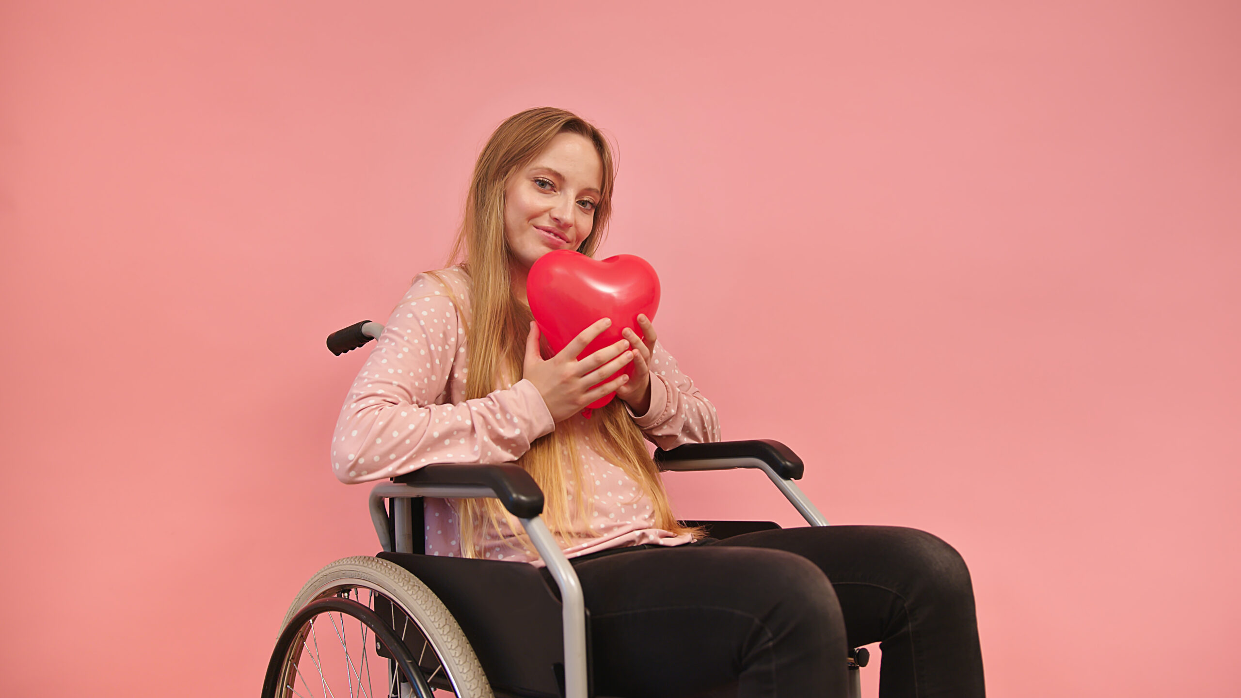 Young caucaian disabled woman in wheelchair holding heart balloon