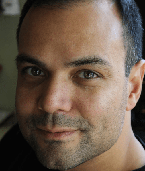 Advisory Board Member Rich Fernandez, with short dark hair and stubble, smiles subtly while looking directly at the camera.