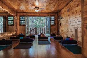 A cozy wooden yoga studio with mats, bolsters, and open doors for grounding practices under the serene Harvest Moon.