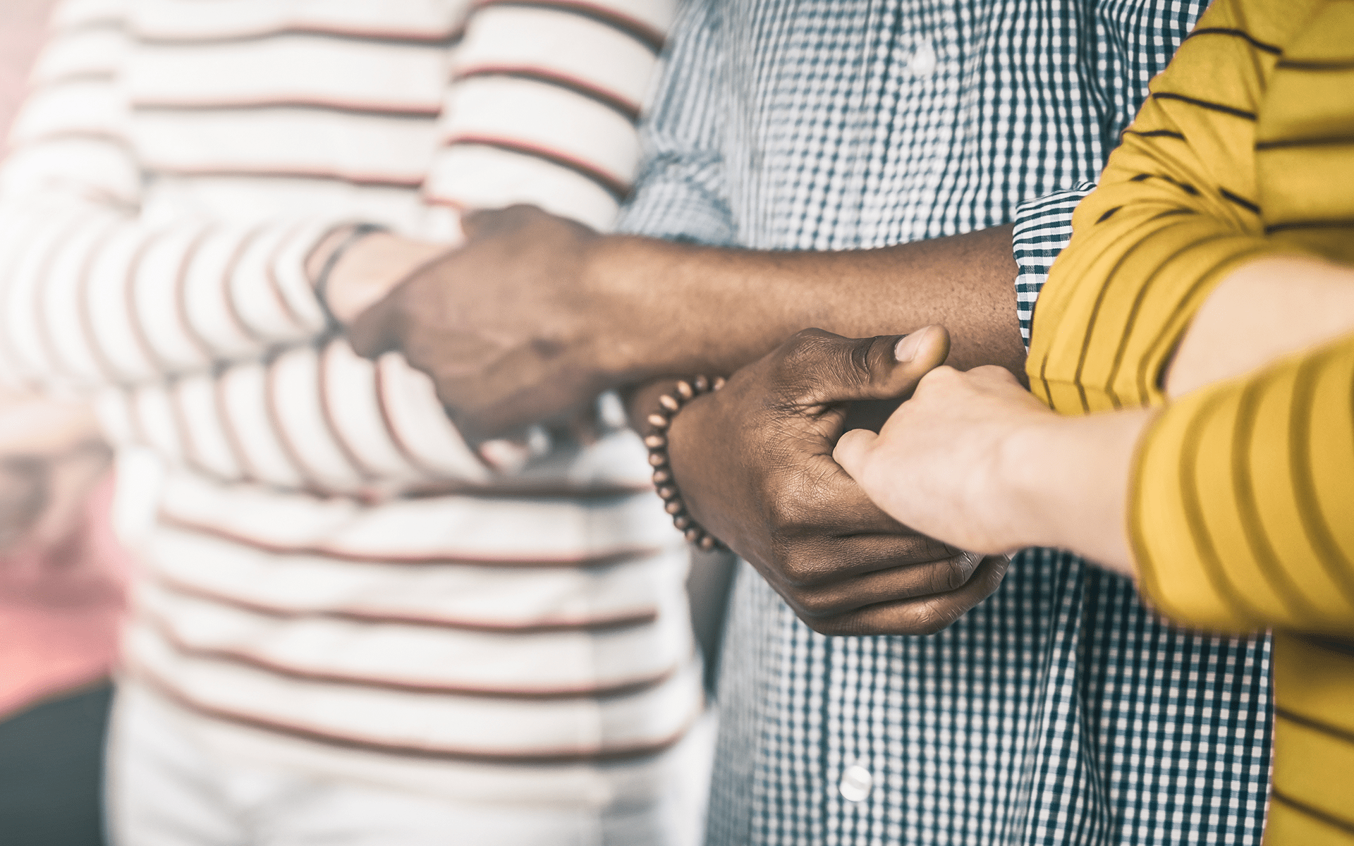 A 12-Minute Meditation for Remembering That We Belong to Each Other-A diverse group of people cross their arms, holding hands with the people next to them.