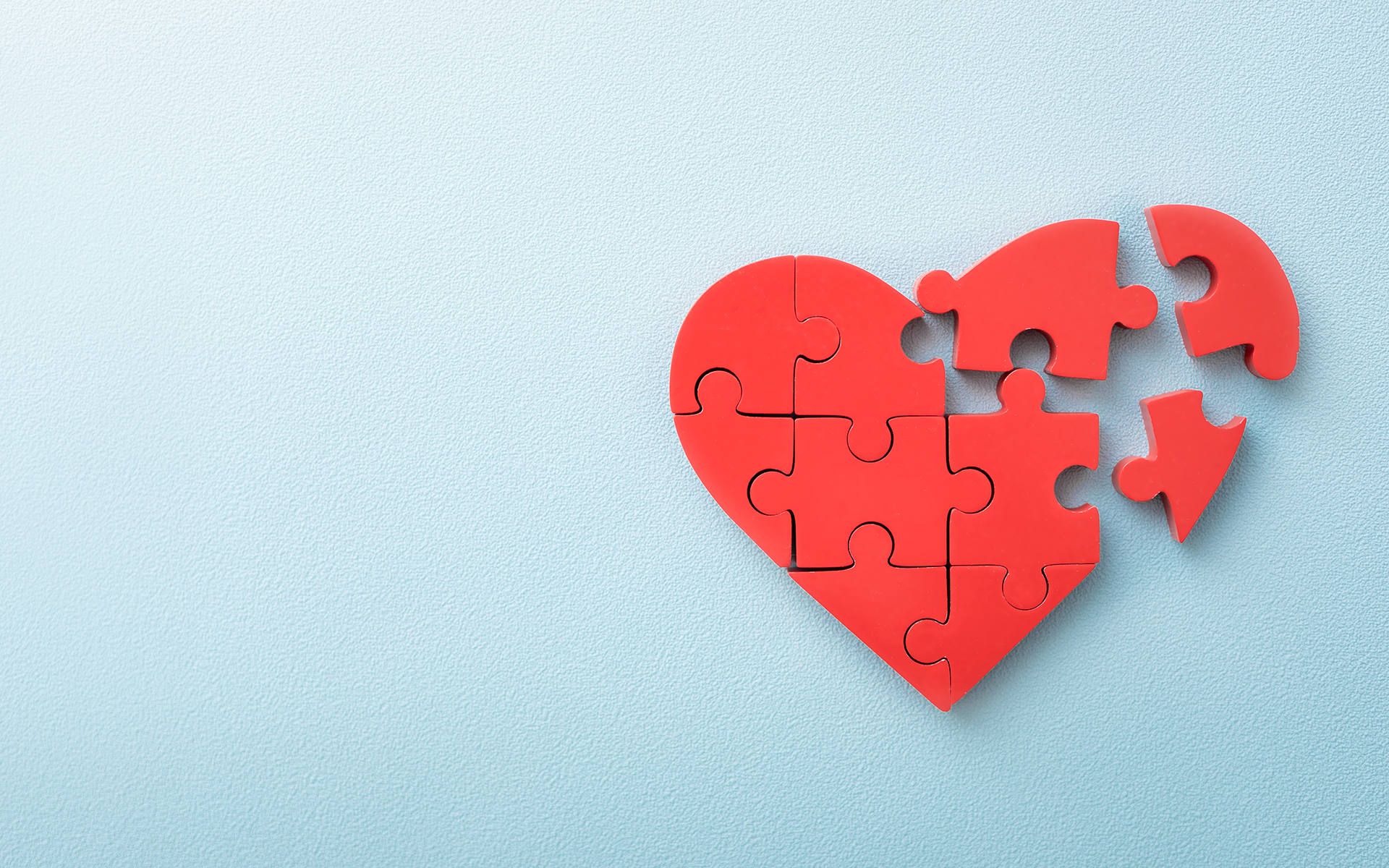 A 12-Minute Meditation to Foster Compassion—A red puzzle fits together in the shape of a heart on a plain light blue background.