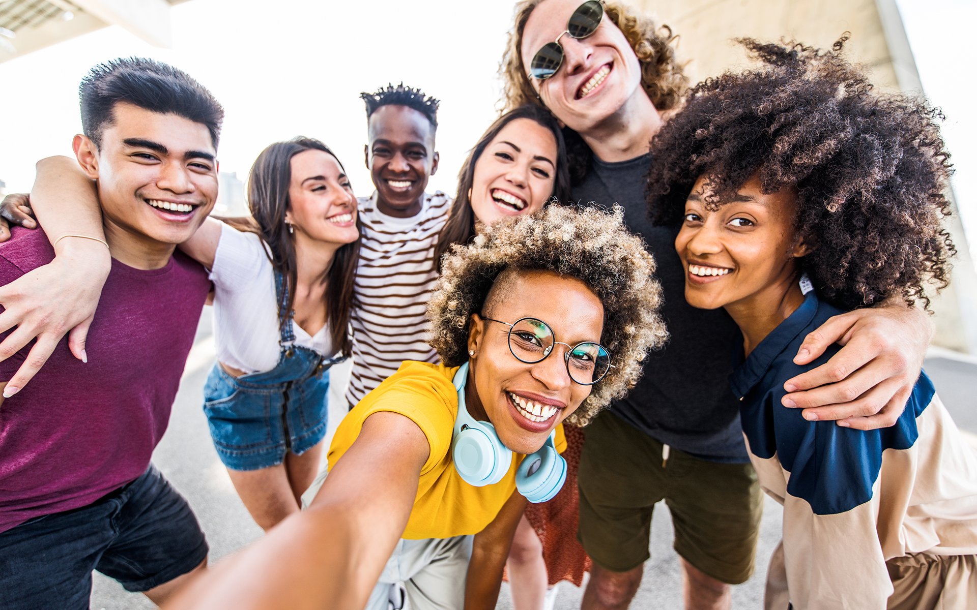 Photo of a diverse group of teenagers with their arms around one another crowding in for a group selfie.