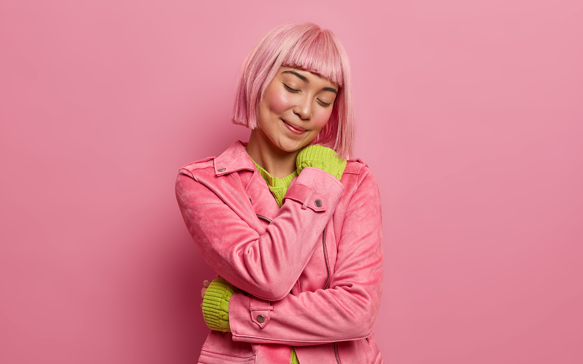 12 Minute Meditation: A Guided Practice to Cultivate Kinder Self-Talk—photo of a young woman with pink hair and a pink jacket on giving herself a hug.