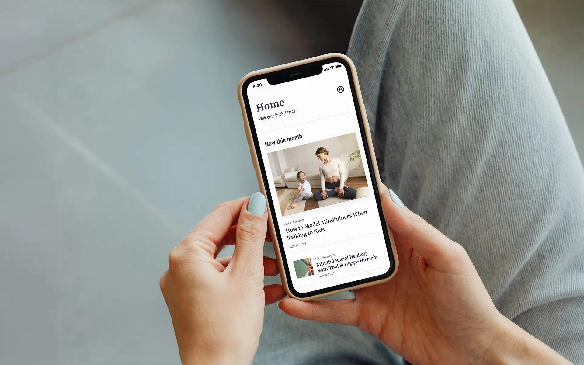 A person holding a smartphone displaying the Mindful app home screen, showing featured articles including How to Model Mindfulness When Talking to Kids