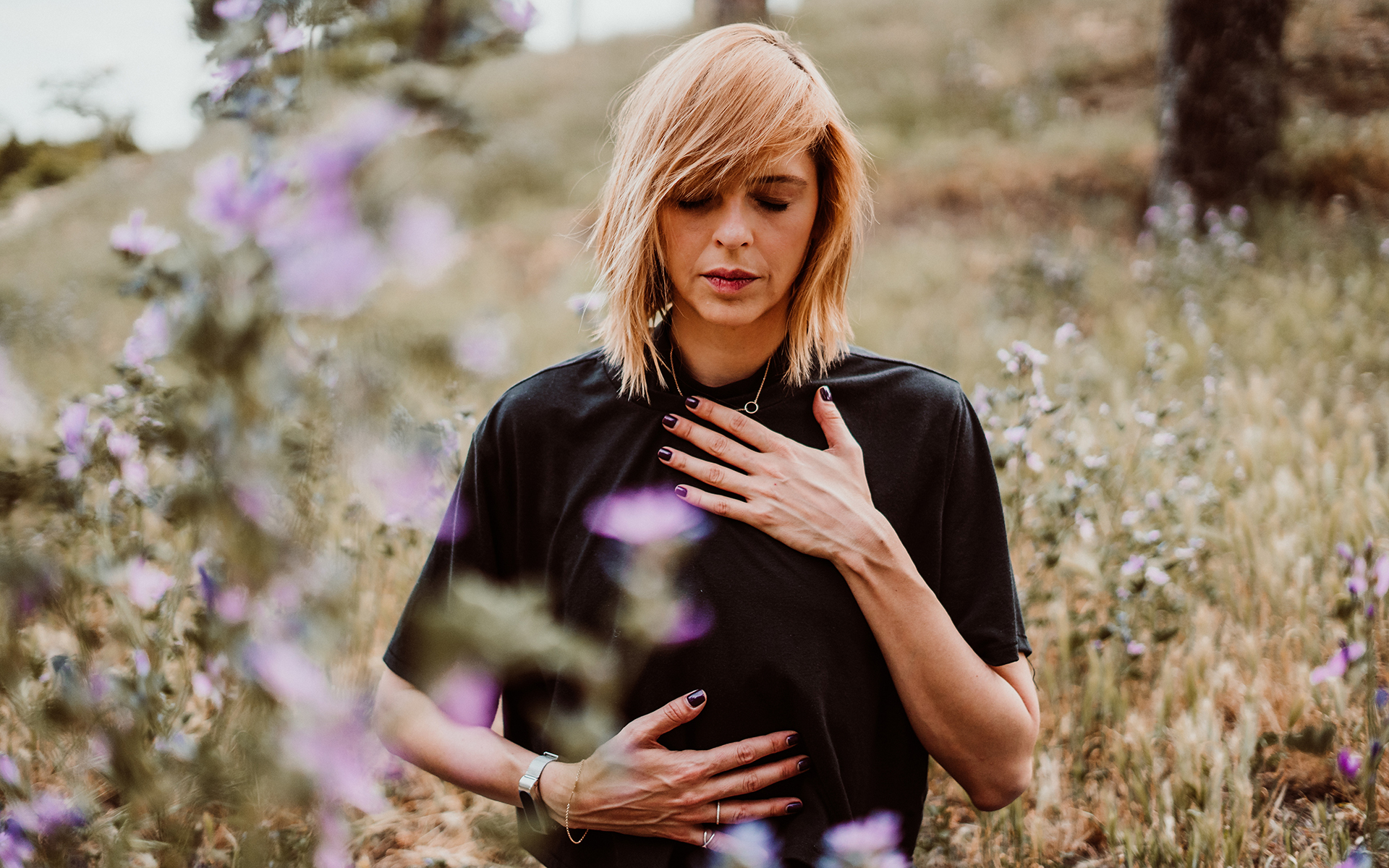 Calming a Rush of Reactivity with Compassion - A blonde woman standing in the middle of a field with one hand on her heart and one hand on her chest
