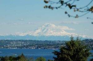 Snow-capped mountain under a blue sky, seen across a lake with trees and a town—an invitation to be Open to Wonder.