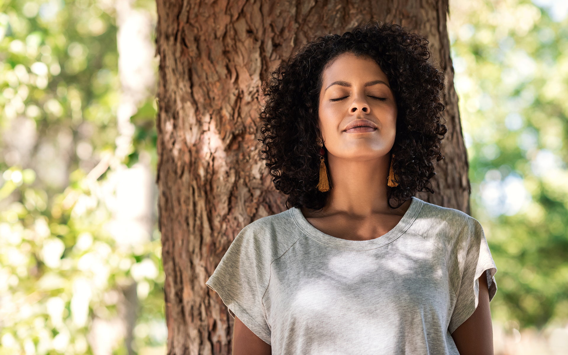 Photo of a Peaceful woman leaning against a tree with her eyes closed