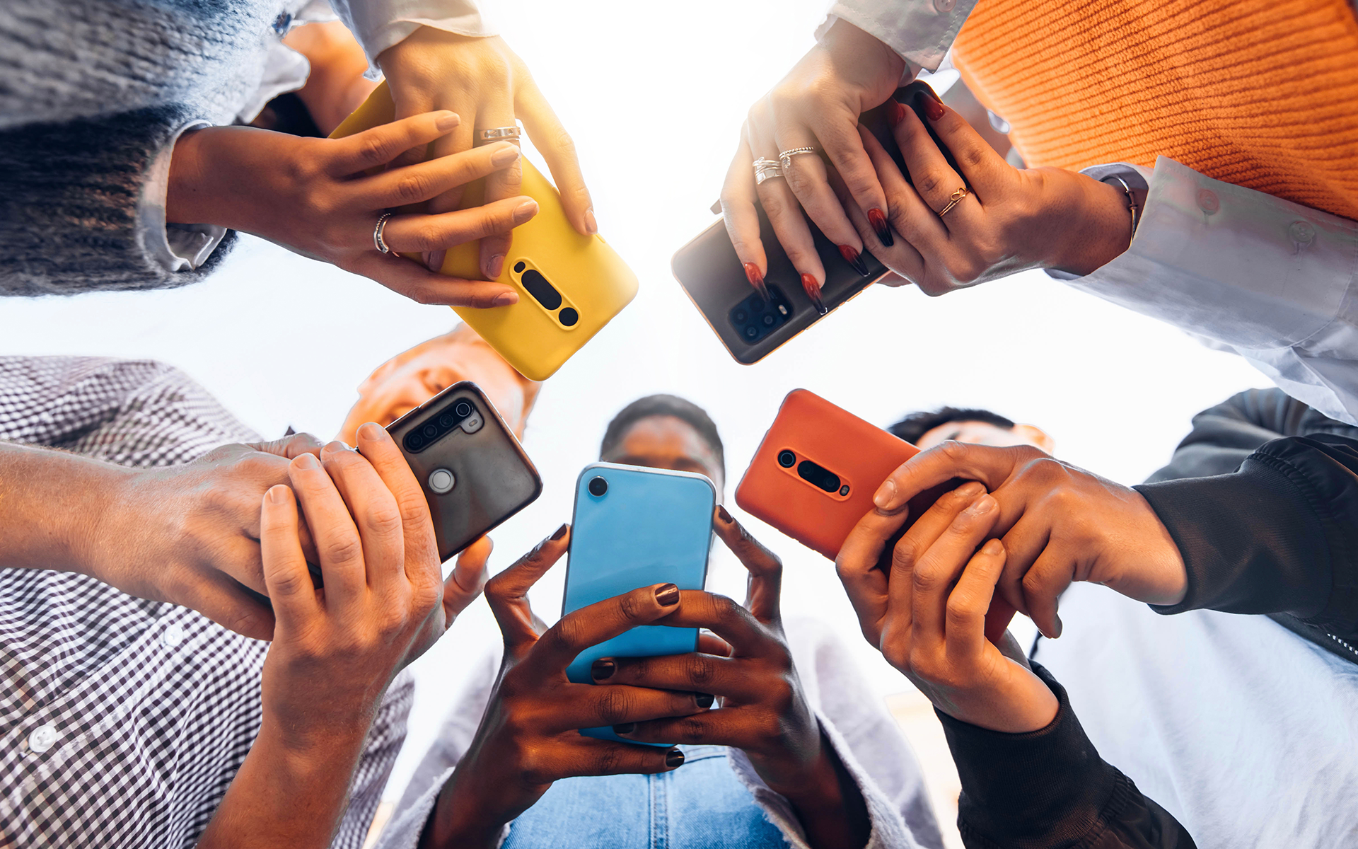 A photo shot facing upwards that captures a circle of diverse teens using their smartphones.