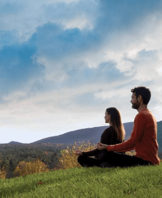 Two people sit cross-legged on grass, meditating outdoors; an inspiring scene for your 2026 Retreat Guide.