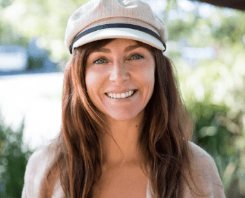 Smiling woman with long brown hair in a light cap, standing outdoors in sunlight for the 2026 Annual Issue.