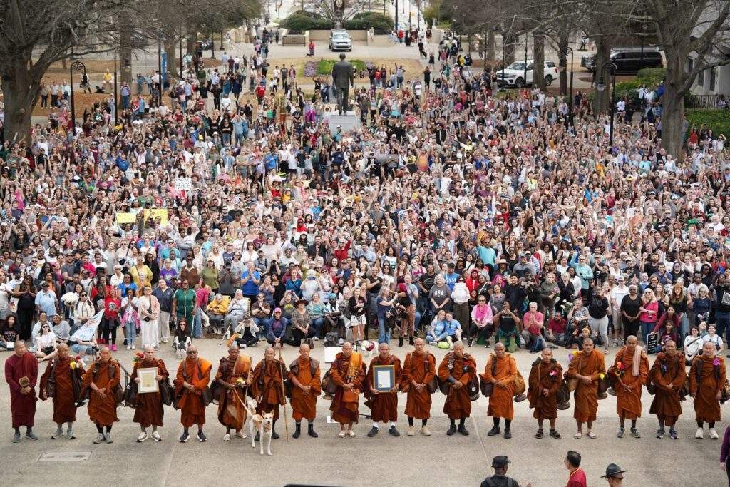 A large crowd gathers behind monks in orange robes at a Walk for Peace outdoor event, united to reimagine peace together.