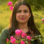 A woman with long dark hair posing outdoors among pink bougainvillea flowers.
