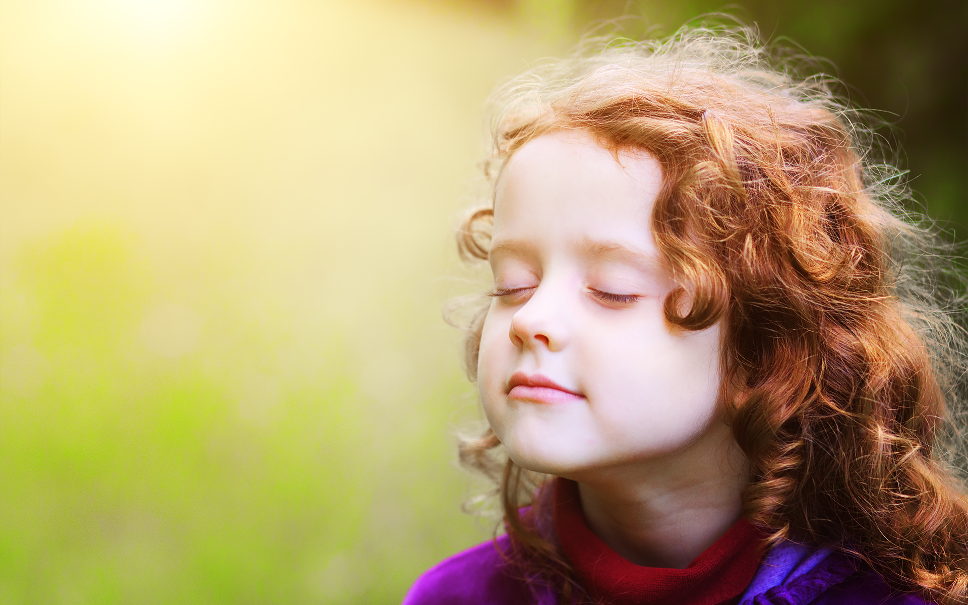 Photo of a little girl with red hair standing outside with her eyes closed, taking a deep breath.