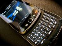 A close-up image of a smartphone with a physical QWERTY keyboard slid out. The screen displays a partial image and a status bar at the top. The device is resting on a dark, textured surface.