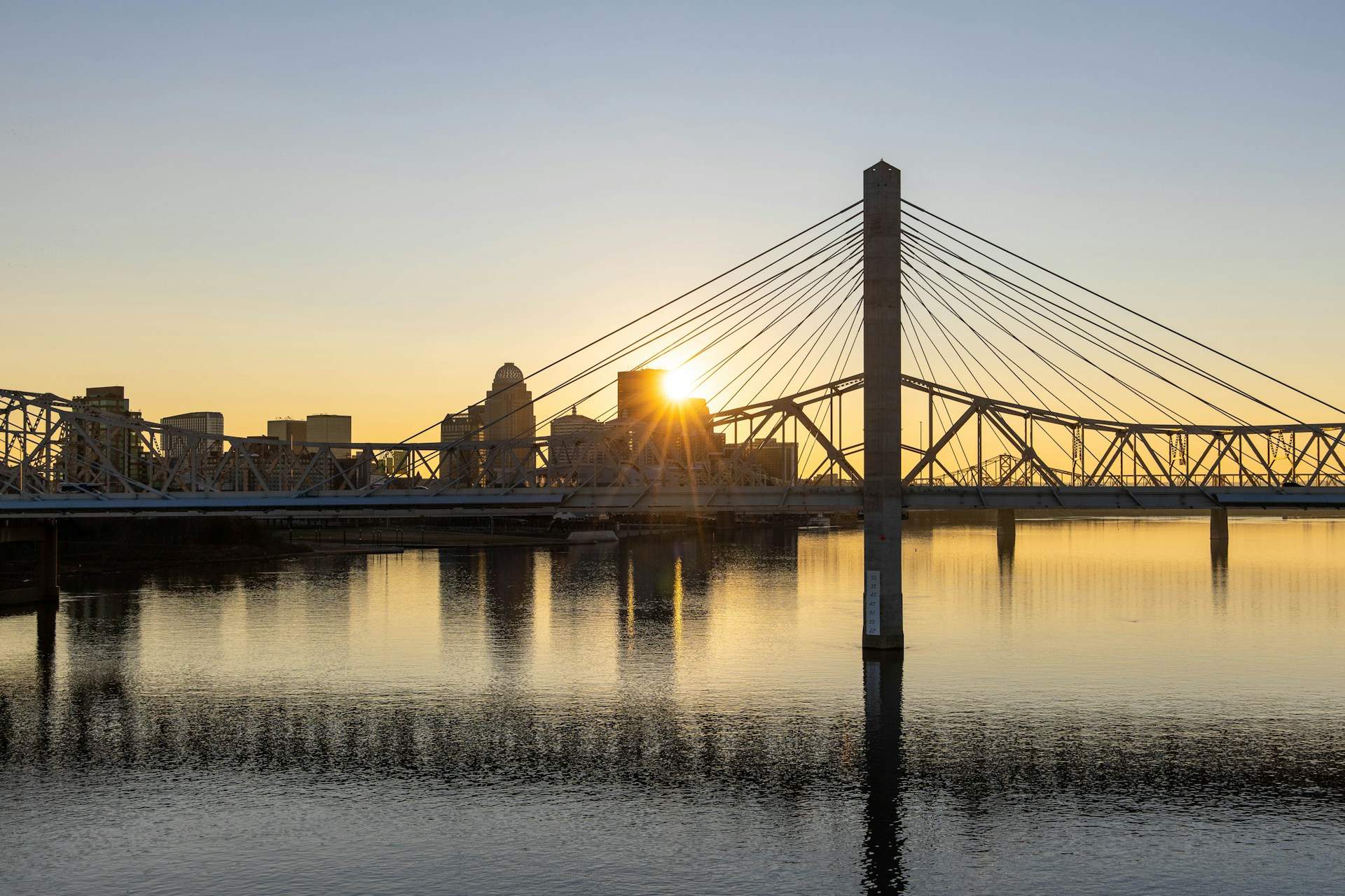 Sunrise over a city skyline, where building a city on compassion bridges communities, reflected on a calm river.