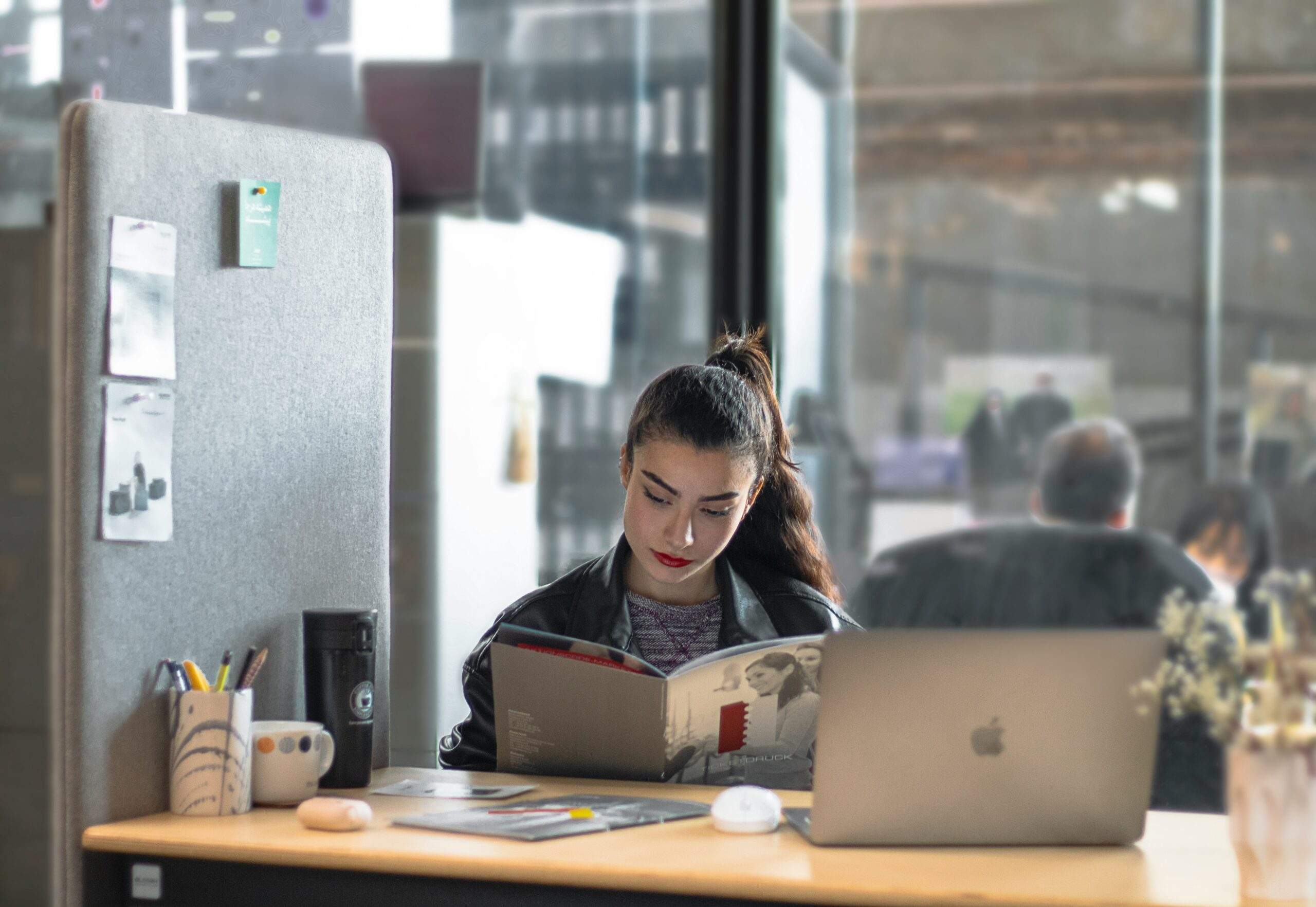 Can mindfulness help us at work? A woman practices mindfulness as she sits at a desk with a laptop, reading a magazine in a modern, open office space.