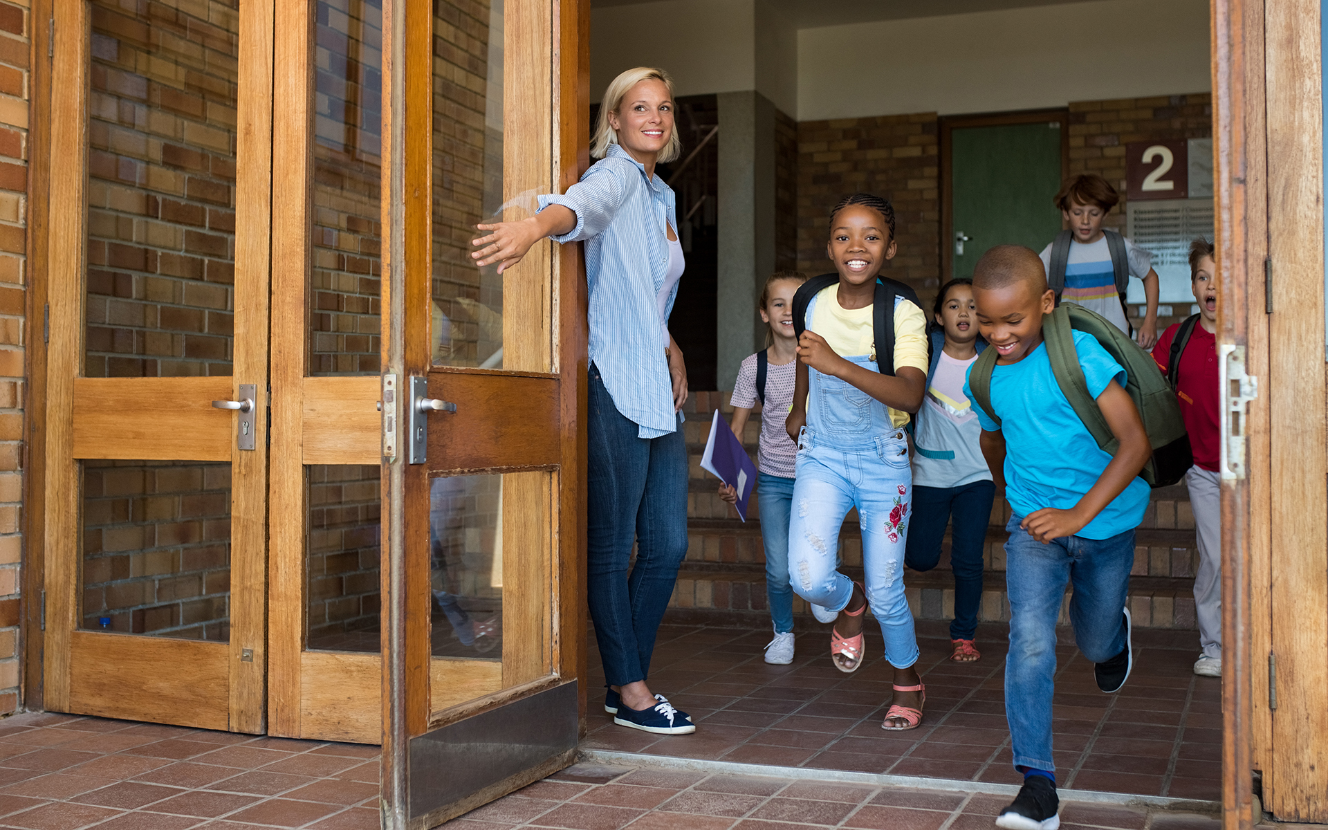 What Mindfulness Brings to an Elementary School Classroom - A teacher holds a classroom door open for students running outside