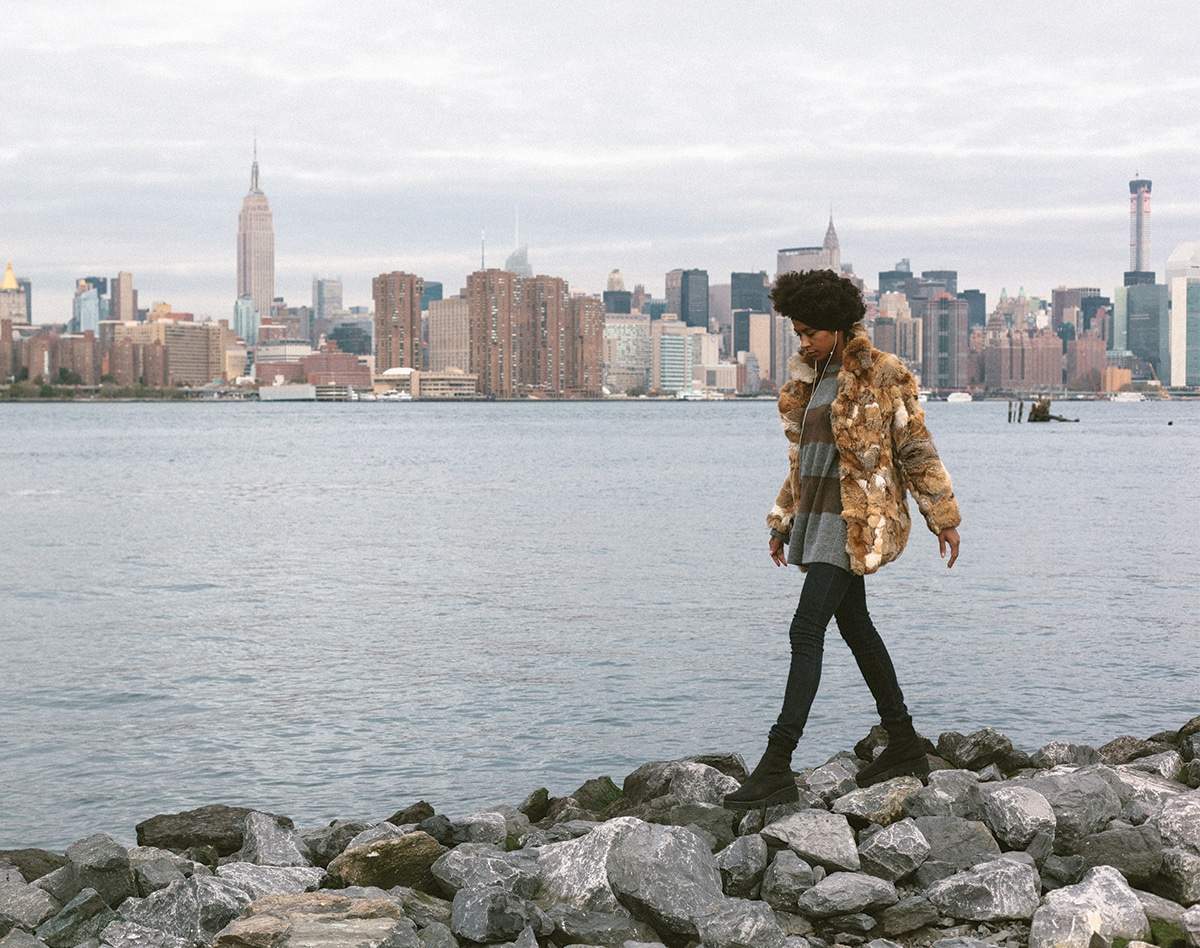 woman in vintage fur coat walking on rocks by ocean