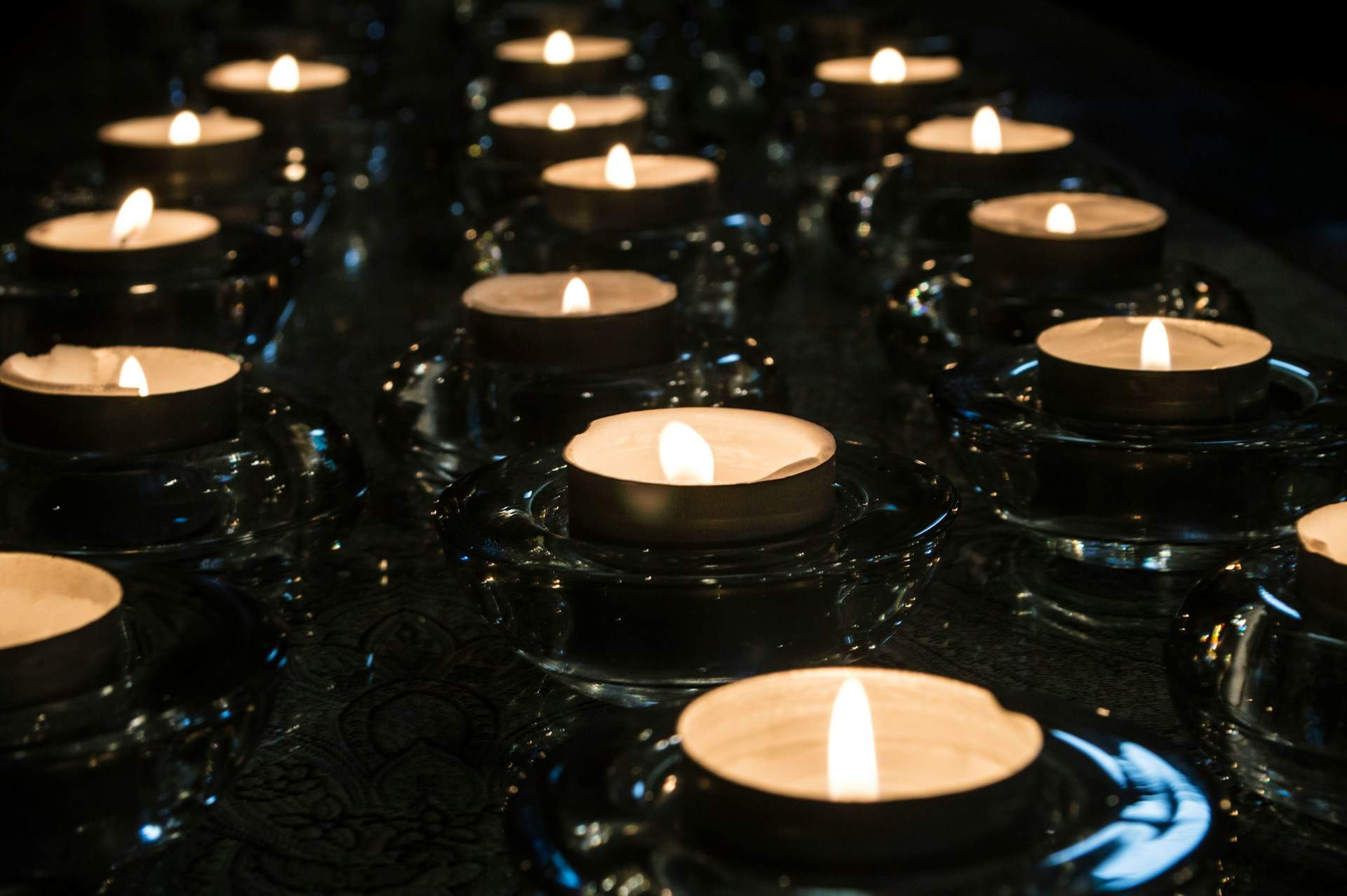 Several lit tealight candles arranged in rows on a dark surface, creating a warm, glowing ambiance—an eco-friendly way to save the planet.