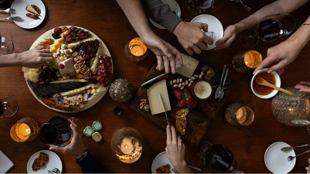 People sharing a cheese platter, fruit, and wine around a candle-lit table, finding comfort after a day marked by vicarious trauma.