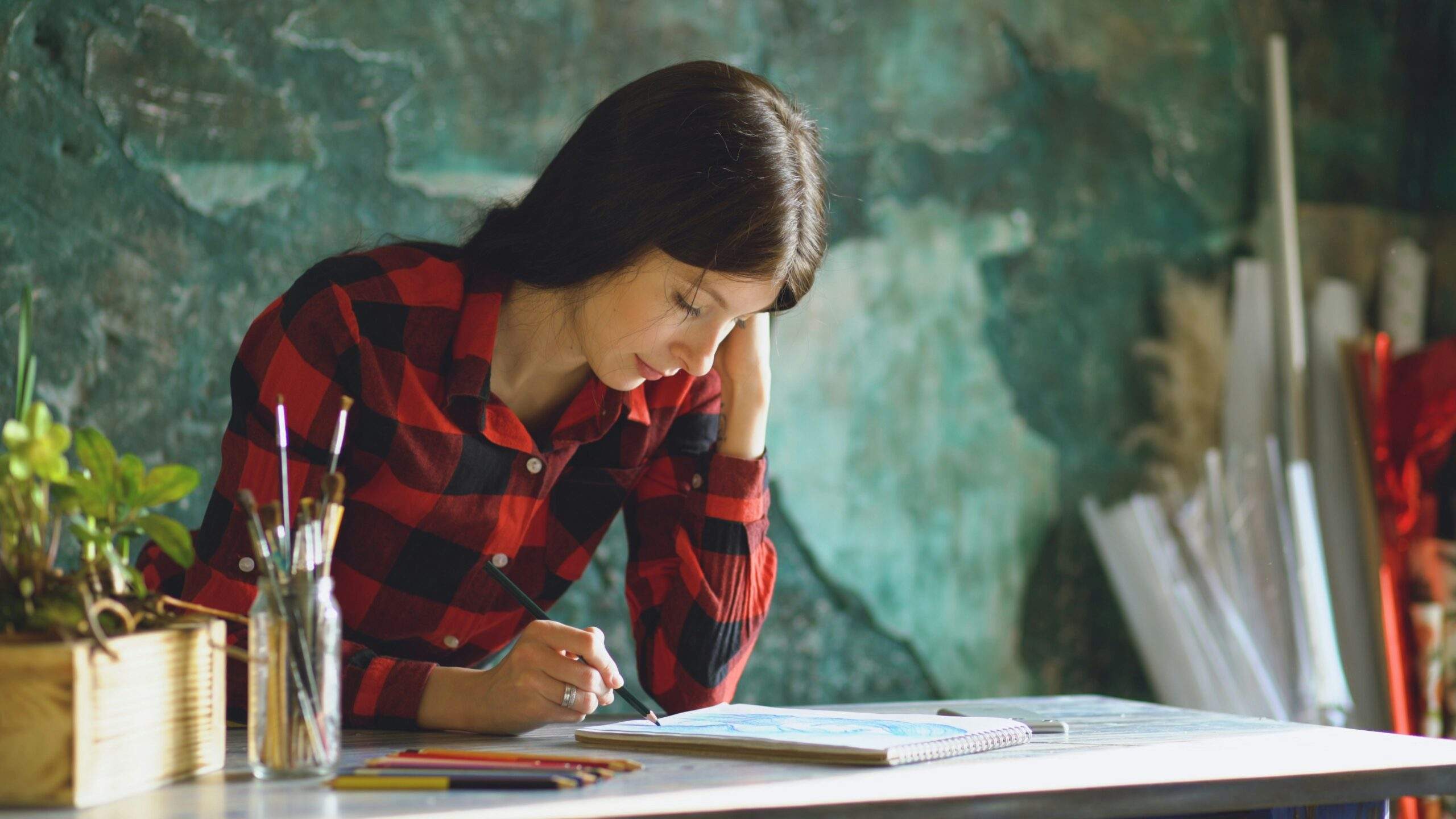 Woman leaning thoughtfully over a sketchbook she's working in. Mindful keys to fostering self-compassion for failure in the creative process.