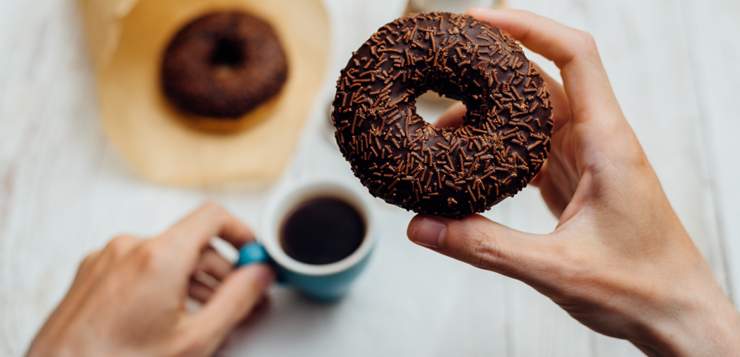 woman eating chocolate donut with her morning coffee