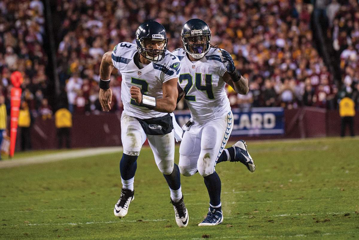 In an unusual move for a star quarterback Russell Wilson, #3, runs interference for running back Marshawn Lynch, #24.