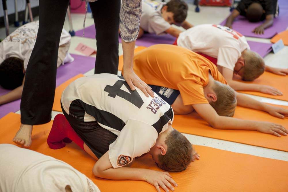 Marian leads the students into child's pose where she touches their backs as a means of reassurance and encouragement during the practice. "We talk about the breath being an anchor, an anchor to their stillness and their steadiness," Marian said. "When they're in child's pose I think that's a really nice place for them to have the anchor of listening to their breath, and I go around and touch students backs and just have kind of a connection to them."