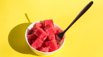 What is Mindful Eating? pieces watermelon in bowl with fork, yellow background