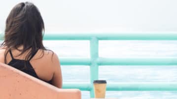 Does Anxiety Make It Hard for You to Focus? Take a Meditation Break woman sitting by water with coffee