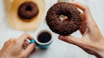 Mindfulness Supports “Wise” Indulgence woman eating chocolate donut with her morning coffee